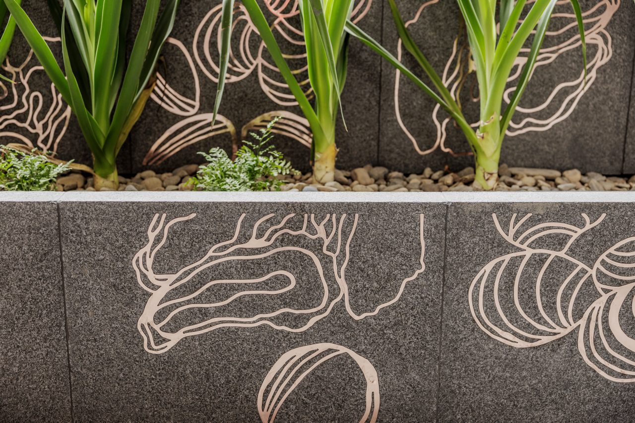 Close-up image of copper artwork inlays in stone, with native landscaping
