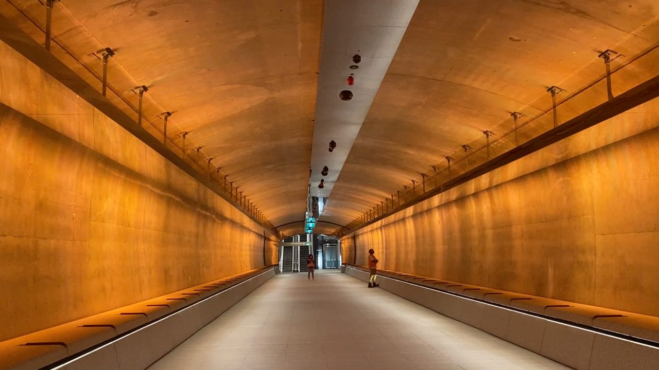 Orange light in pedestrian link tunnel, featuring two people walking through