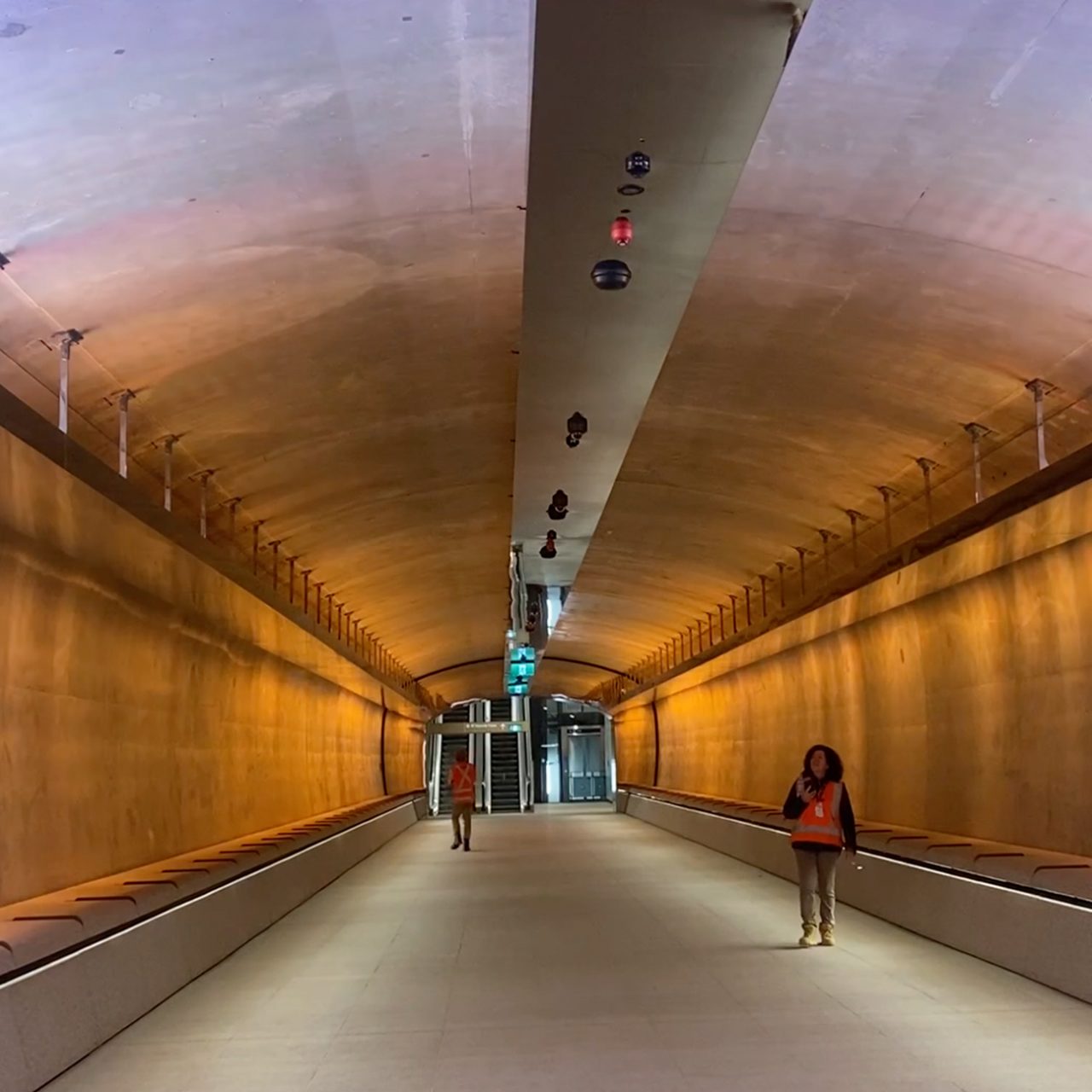 White and orange coloured lights inside the tunnel, featuring two people walking through